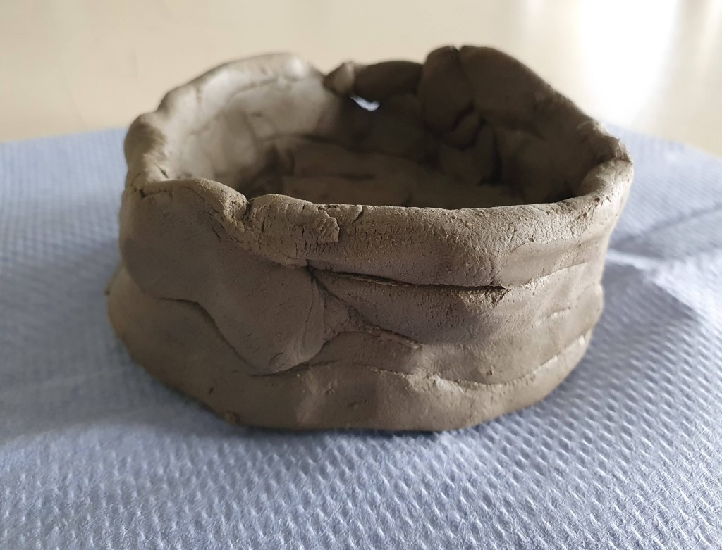 A handmade clay bowl with a rough exterior, resting on a textured surface.
