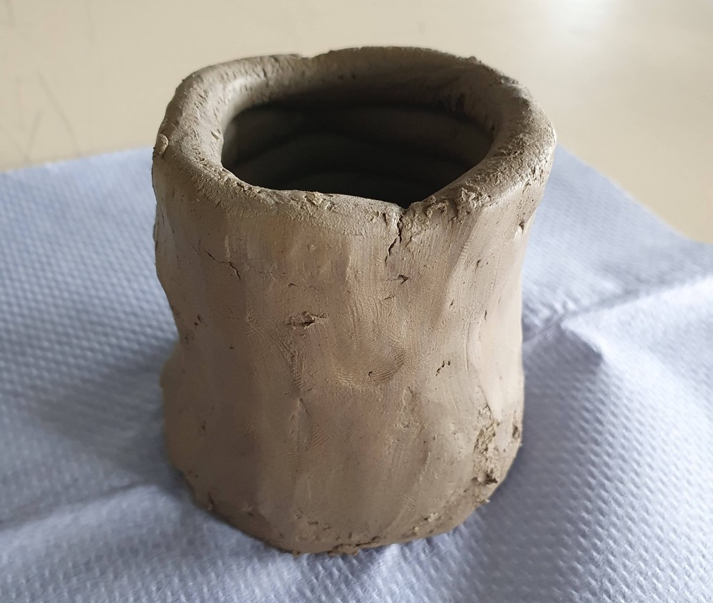 A handmade clay jar or bottle, featuring a textured surface and natural, organic shape, placed on a light-colored cloth.