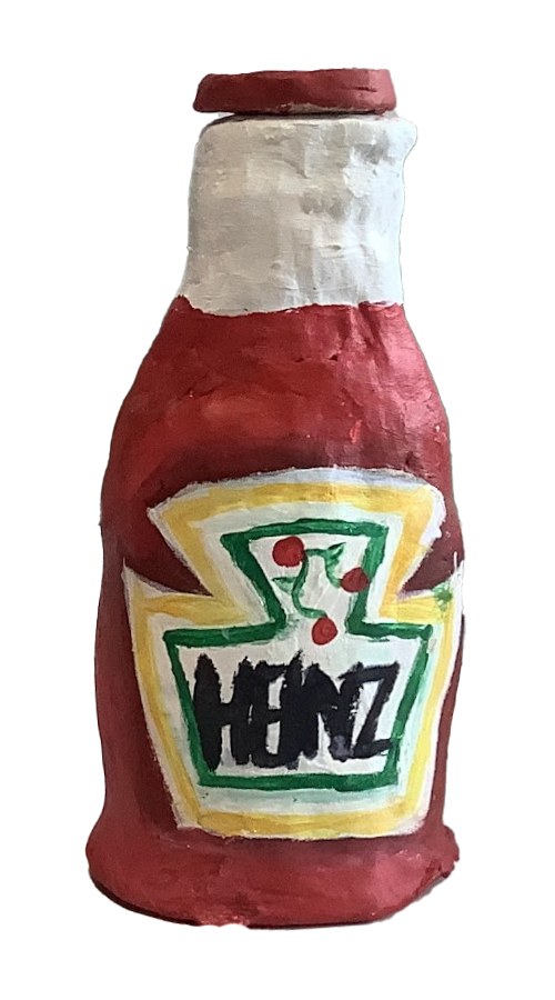 A handmade clay sculpture of a ketchup bottle, featuring a red body, white top, and a painted Heinz label with yellow and green accents.