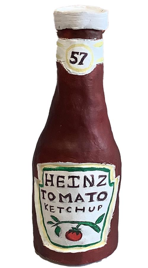 A handcrafted clay model of a Heinz tomato ketchup bottle, painted in red with a white cap and a label featuring the iconic logo.