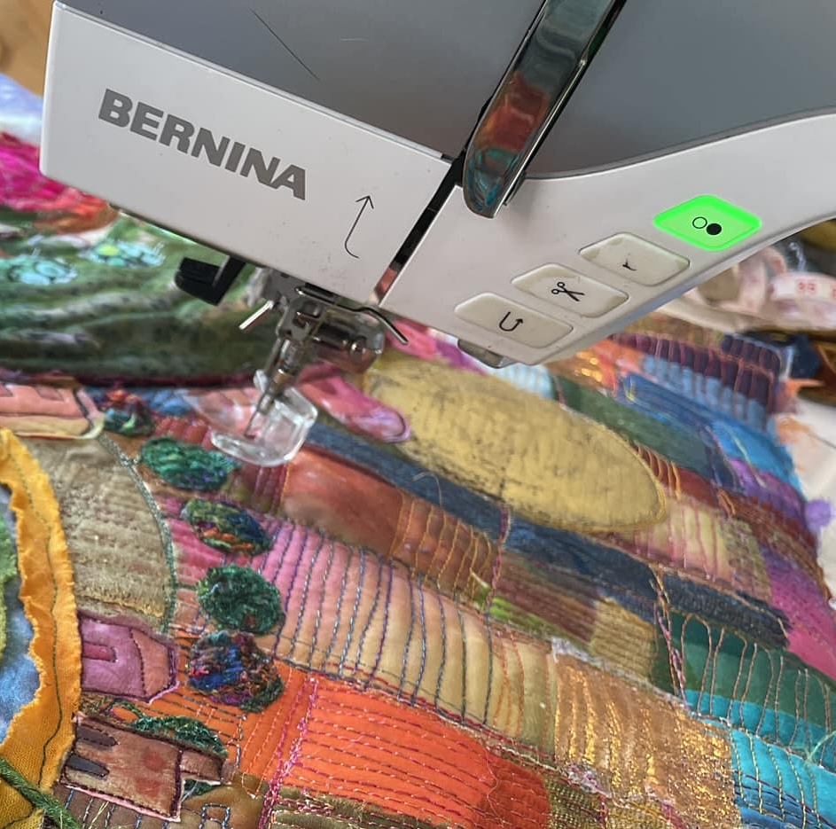 Close-up of a Bernina sewing machine in use, stitching colorful textile art with intricate patterns and textures.