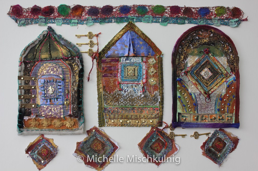 Colorful textile artwork featuring three stylized houses with intricate patterns, textures, and embellishments, accompanied by decorative fabric pieces and keys, showcasing the Michelle Mischkulnig's craftsmanship.