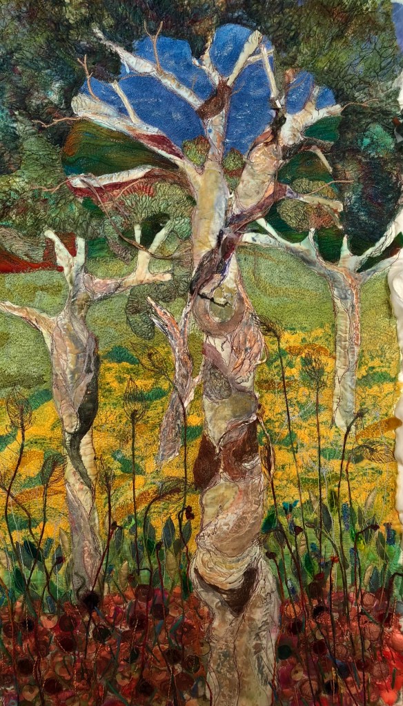 A vibrant textile artwork depicting stylized trees with intricate fabric layers, showcasing a vivid blue sky and a colorful landscape with green and yellow hues. Michelle Mischkulnig