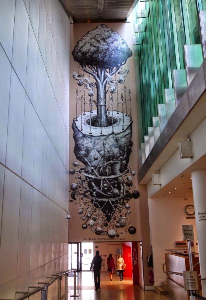 A large, intricate mural by street artist Phlegm depicting a tree growing from a surreal landscape filled with abstract objects and whimsical elements. The artwork combines black and white line work with fantastical themes, transforming the urban space into a dreamlike environment.