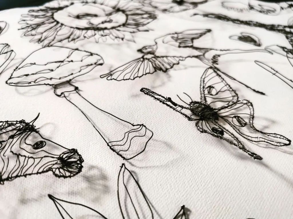 A close-up view of intricate wire sculptures depicting various nature-inspired elements, including a sunflower, birds, and a butterfly, showcasing fluid lines and fine details.