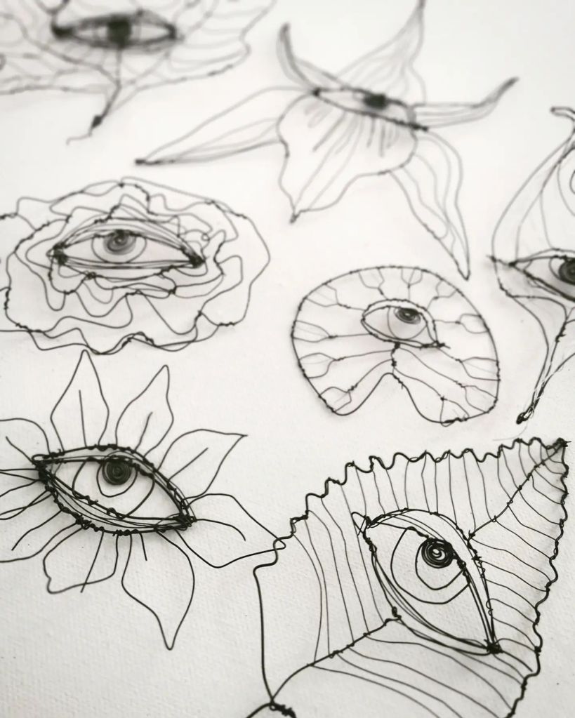 A collection of wire art depicting stylized flowers and eyes, showcasing intricate line work and detailed layering.