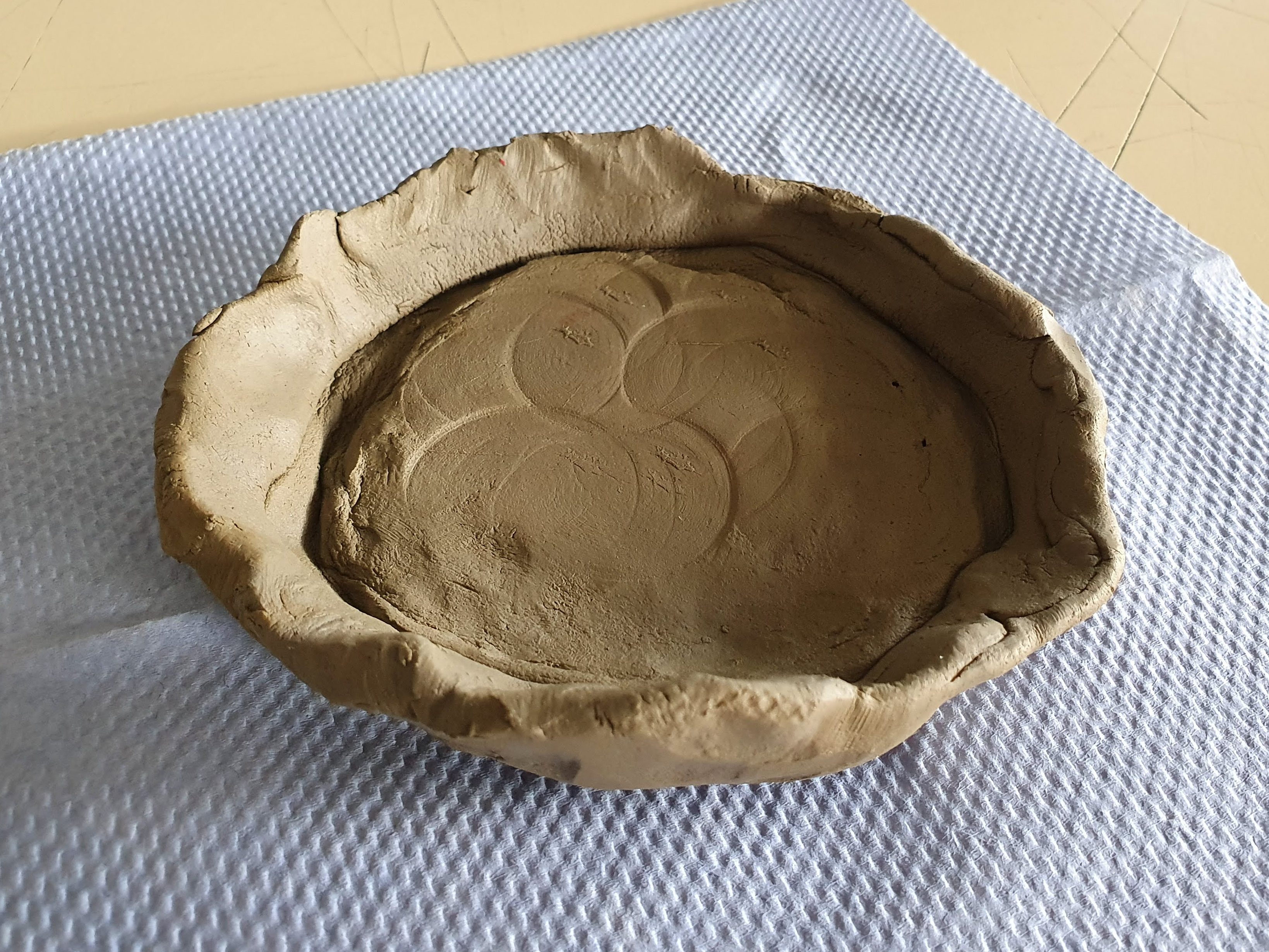 A handmade clay bowl with a textured design on the bottom, resting on a blue cloth surface.