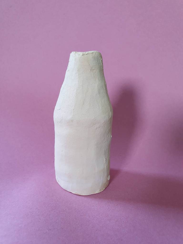 A simple, unglazed clay bottle with a narrow neck, placed against a pink background.