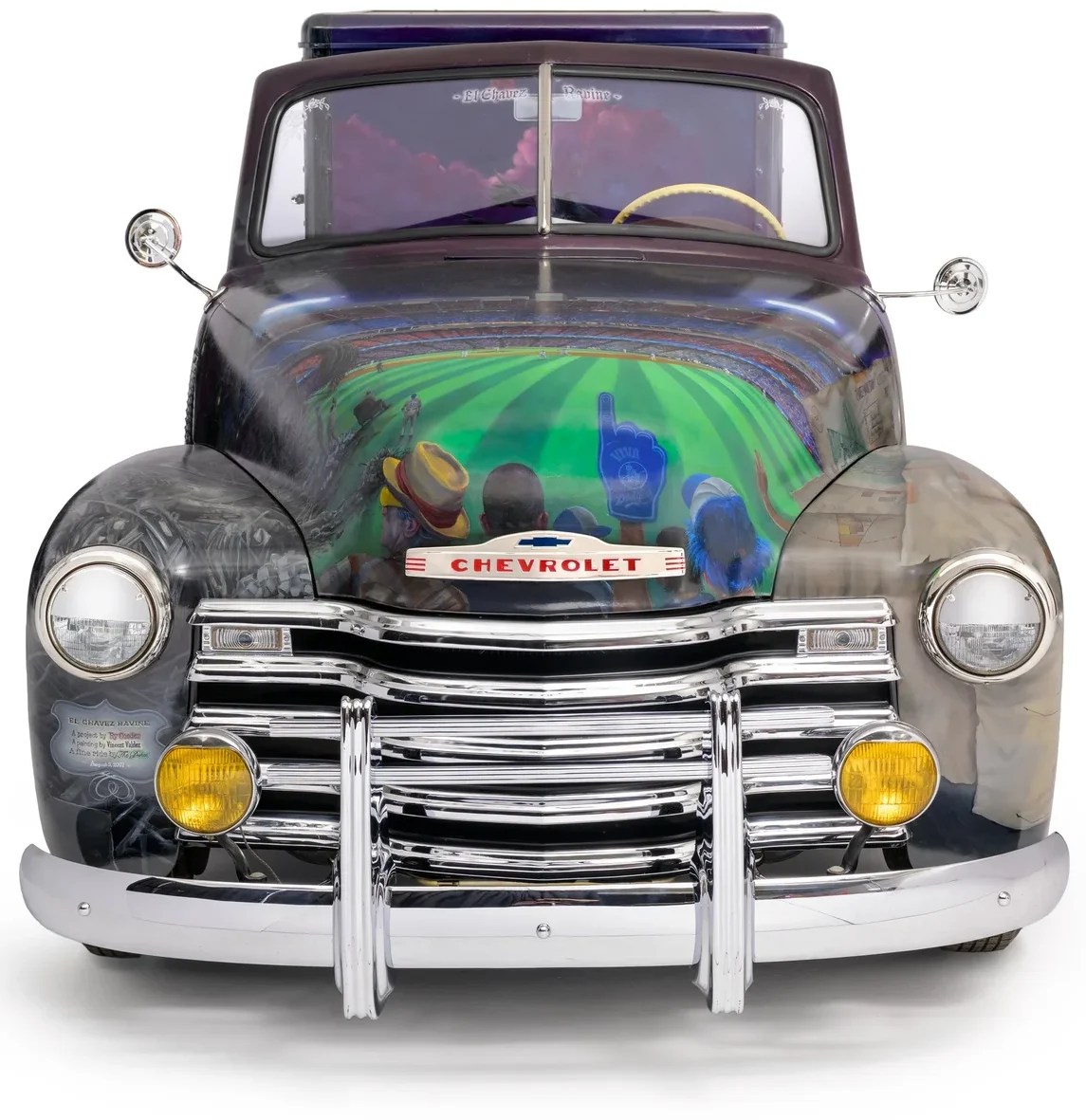 Front view of a classic Chevrolet truck, featuring detailed chrome grille and headlights, with a colorful mural depicting a sports scene on the hood.