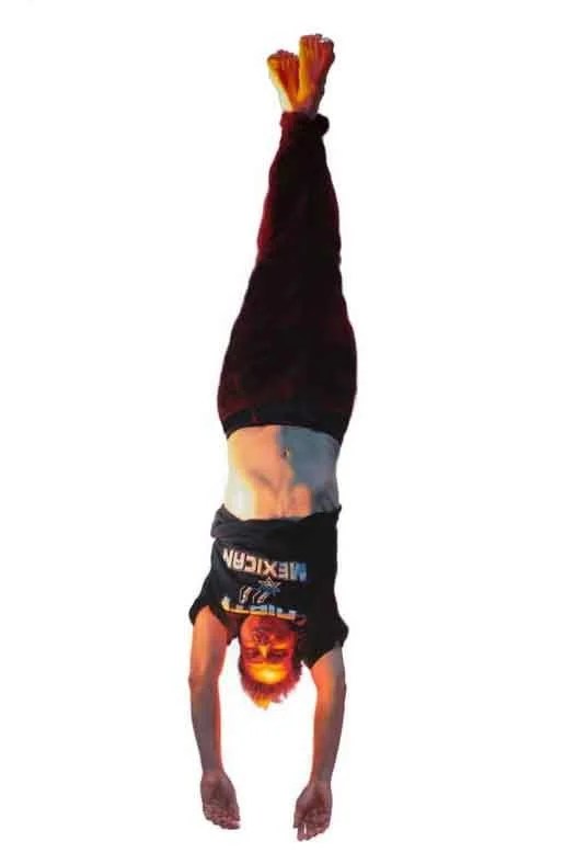 Person performing a handstand with arms extended and legs together, wearing a black T-shirt and dark pants, against a white background.