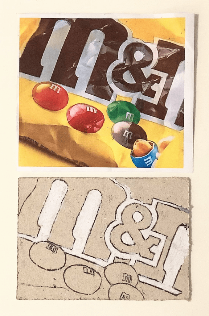 A printed image of M&M's packaging featuring colorful candies on a yellow background, accompanied by a monoprinted sketch of the same design on cardboard.
